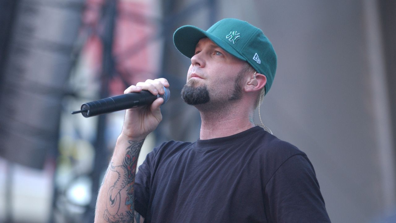 Fred Durst looking solemn on stage in a green cap